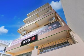 Un edificio de varios pisos con balcones, un cartel que dice 'Hotel Ashirwad Guest House' y la marca 'OYO'.
