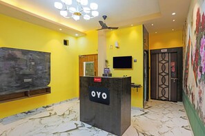 Una recepción con un letrero que dice 'OYO' en el vestíbulo de un hotel con paredes amarillas, un ventilador de techo y una puerta con diseño decorativo.