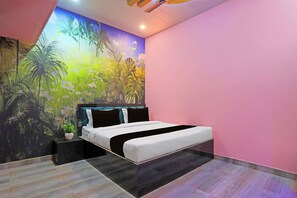 A modern bedroom with a bed, a nightstand, a potted plant, and a mural of tropical foliage on the wall. - Hotel O by OYO The Baba Guest House (Varanasi)
