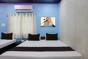Habitación de hotel con cama, dos mesitas de noche, teléfono, planta y ventana con cortinas.