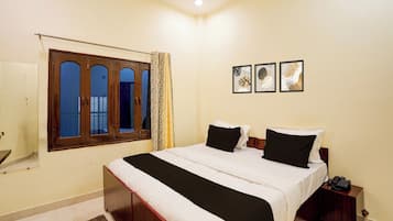 Une chambre à coucher avec un lit, une table de chevet, un téléphone et une fenêtre avec des rideaux.