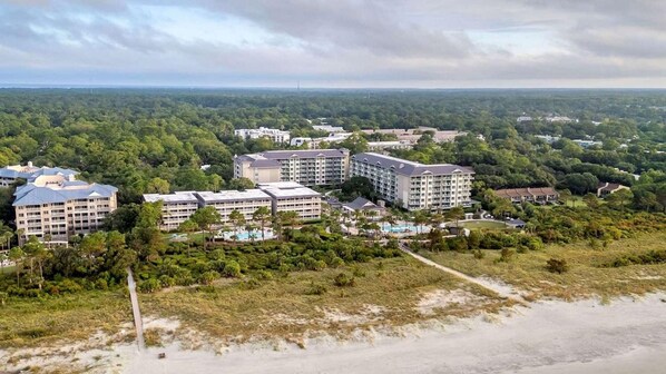 Un complexe hôtelier comprenant plusieurs bâtiments, dont un grand hôtel avec piscine et un bâtiment plus petit offrant une vue sur la plage.