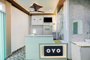 Ein Empfangsbereich mit einer Rezeption, einem Deckenventilator, einem Fernseher und einem Empfangsschild.