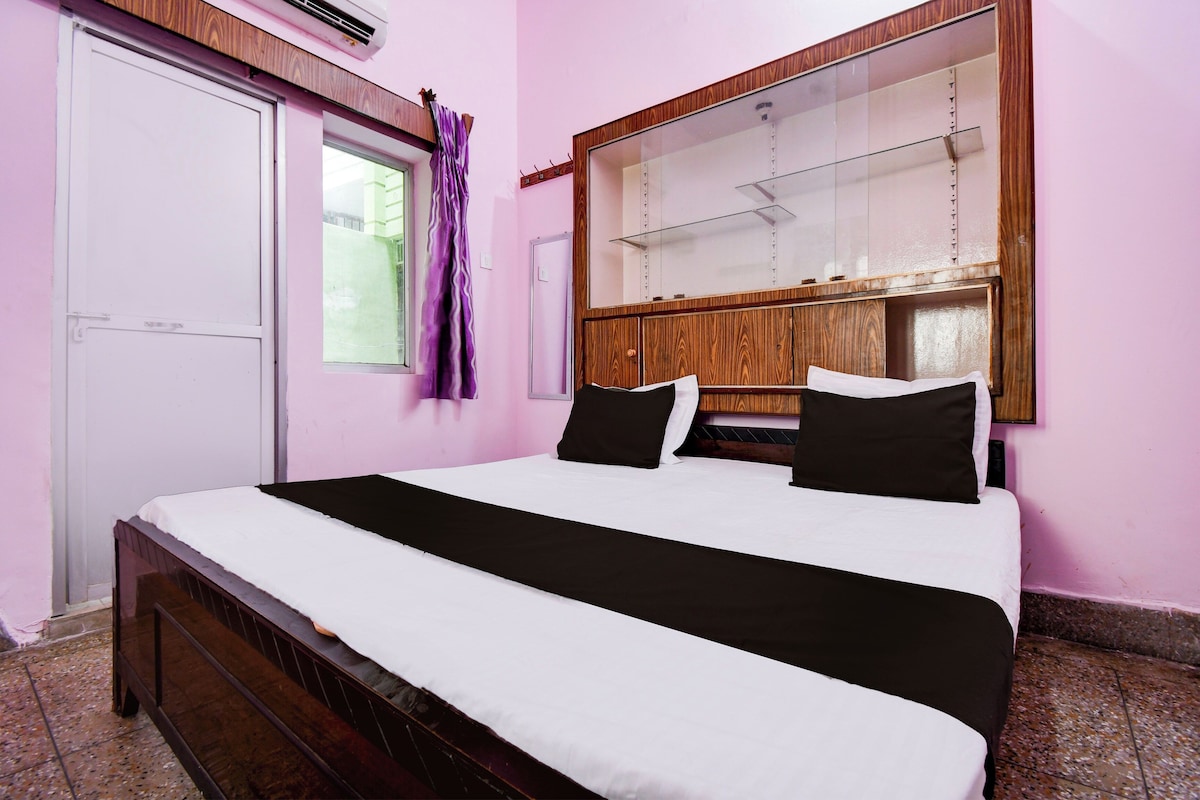 Une chambre à coucher avec un lit, une fenêtre avec des rideaux, une tête de lit en bois et un climatiseur fixé au mur.