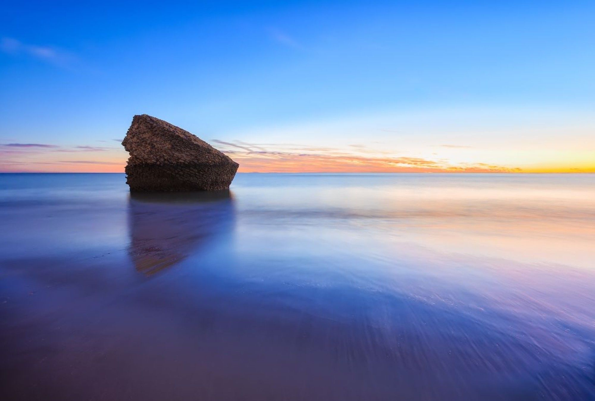 A rock formation in the ocean with a clear sky.