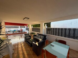 Un espace extérieur aménagé en terrasse, avec un sol carrelé, des meubles en osier et une table en verre.