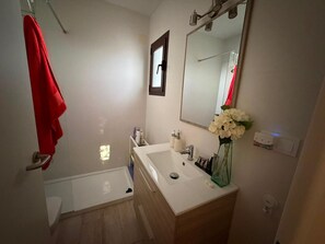 Une salle de bain moderne avec un lavabo blanc, un miroir et une serviette rouge accrochée à la porte.