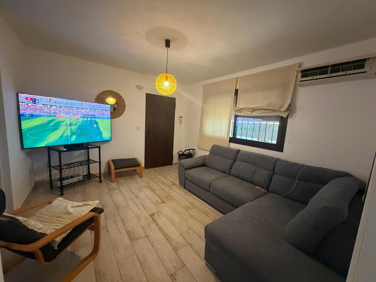 Una sala de estar con televisión, un sofá, una silla y piso de madera.