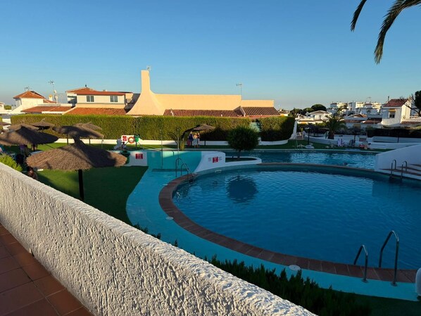 Una piscina de borde curvo, rodeada por un muro blanco y un seto.