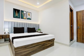 A modern bedroom with a bed, bedside tables, a nightstand, a wall-mounted lamp, and framed artwork. - Hotel O Natraj Paying guest house (Varanasi)