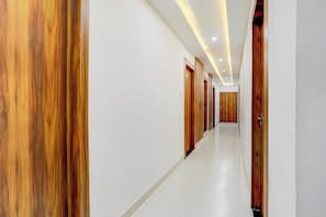 A long, narrow hallway with wooden doors on one side and white walls on the other. - Hotel O Natraj Paying guest house (Varanasi)