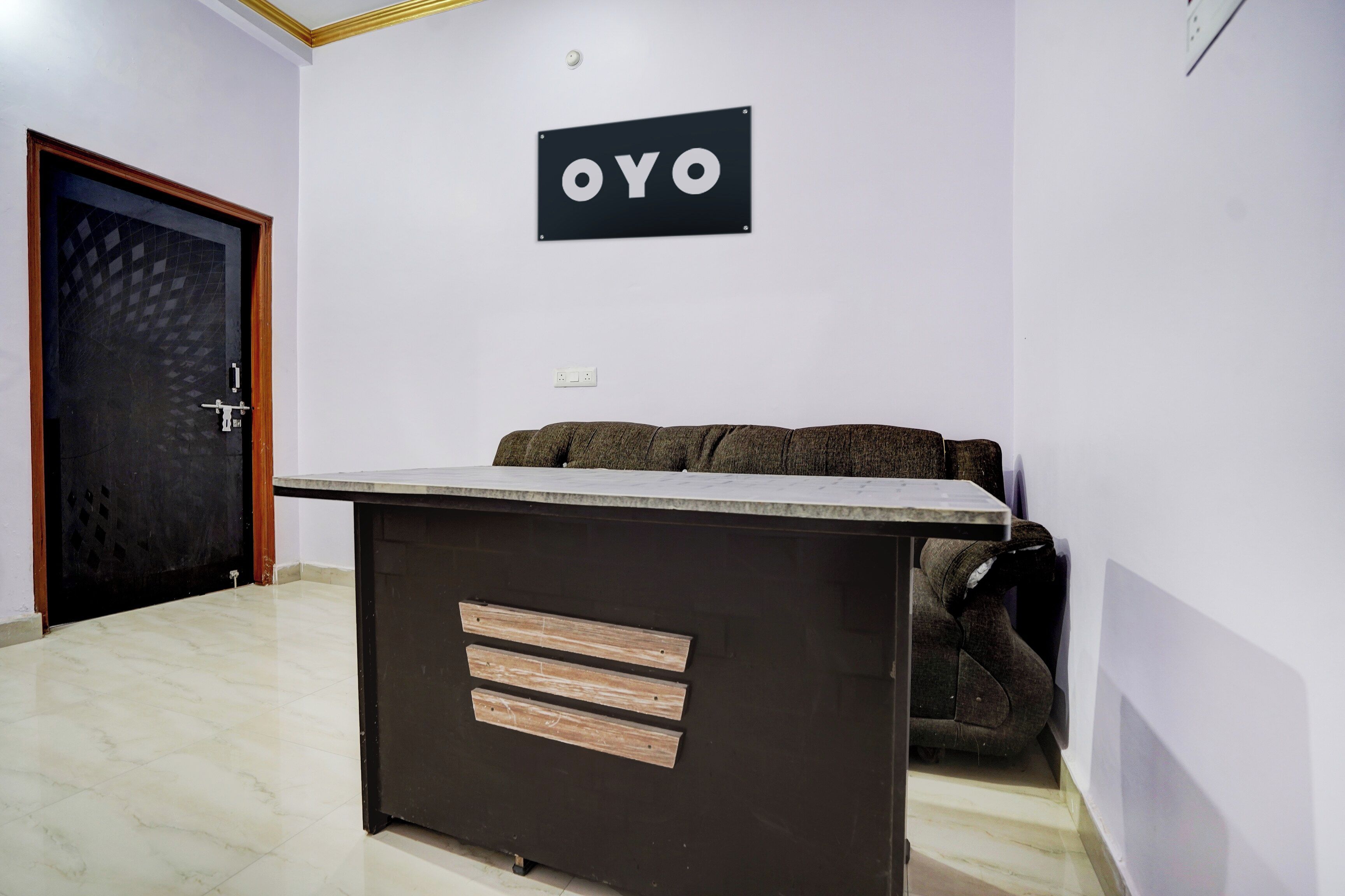 Une pièce comprenant un bureau de couleur sombre, un canapé, une porte et un panneau fixé au mur avec les lettres « OYO ».