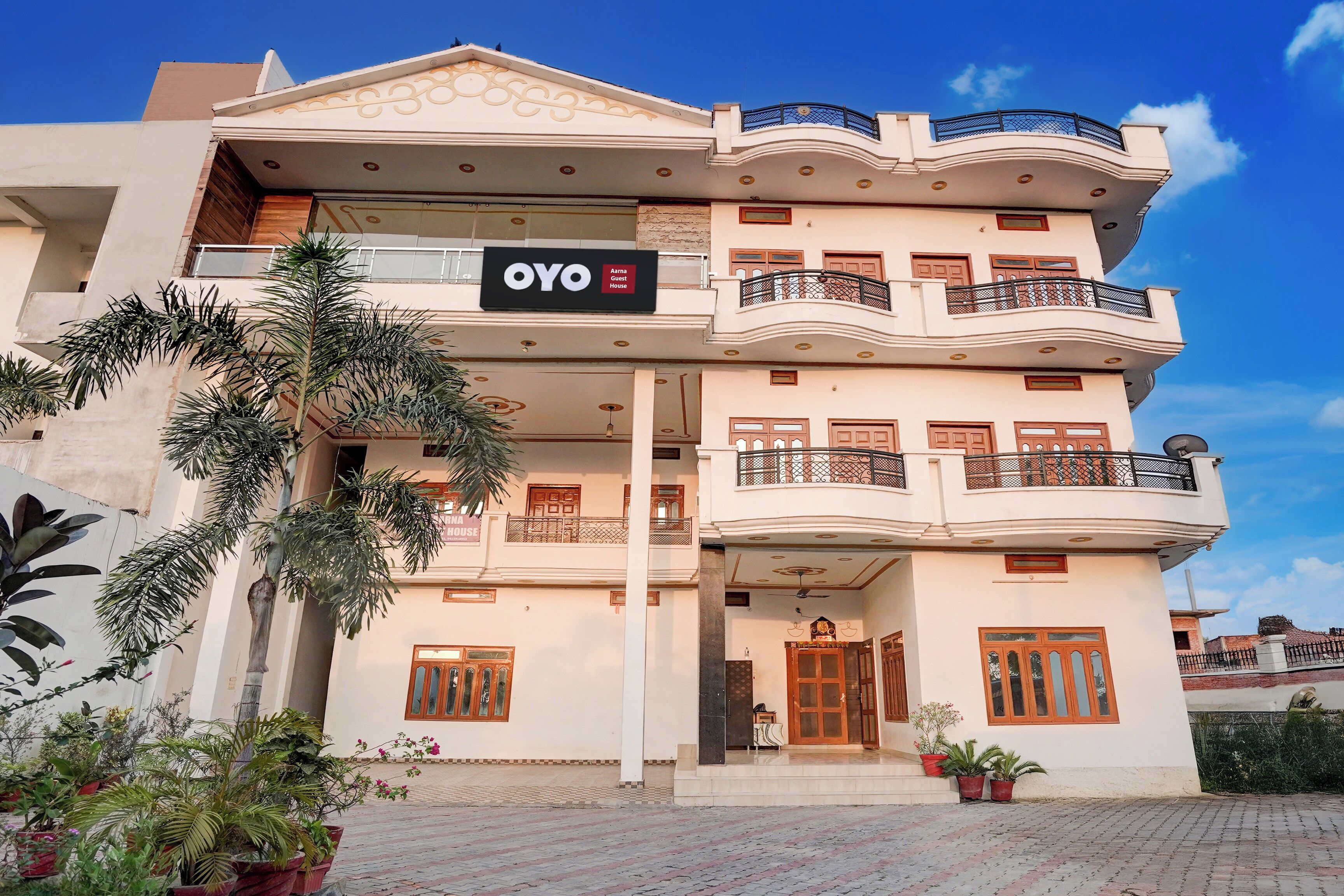 Un immeuble à plusieurs étages doté de balcons, une enseigne indiquant « OYO Aarna Guest House », et des plantes en pot.