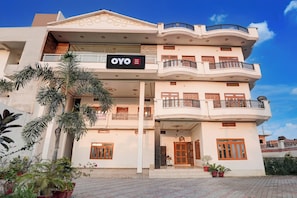 Un edificio de varios pisos con balcones, un letrero que dice 'OYO Aarna Guest House' y plantas en macetas.