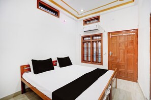 Une chambre à coucher avec un lit, une porte en bois et une fenêtre avec des barreaux.