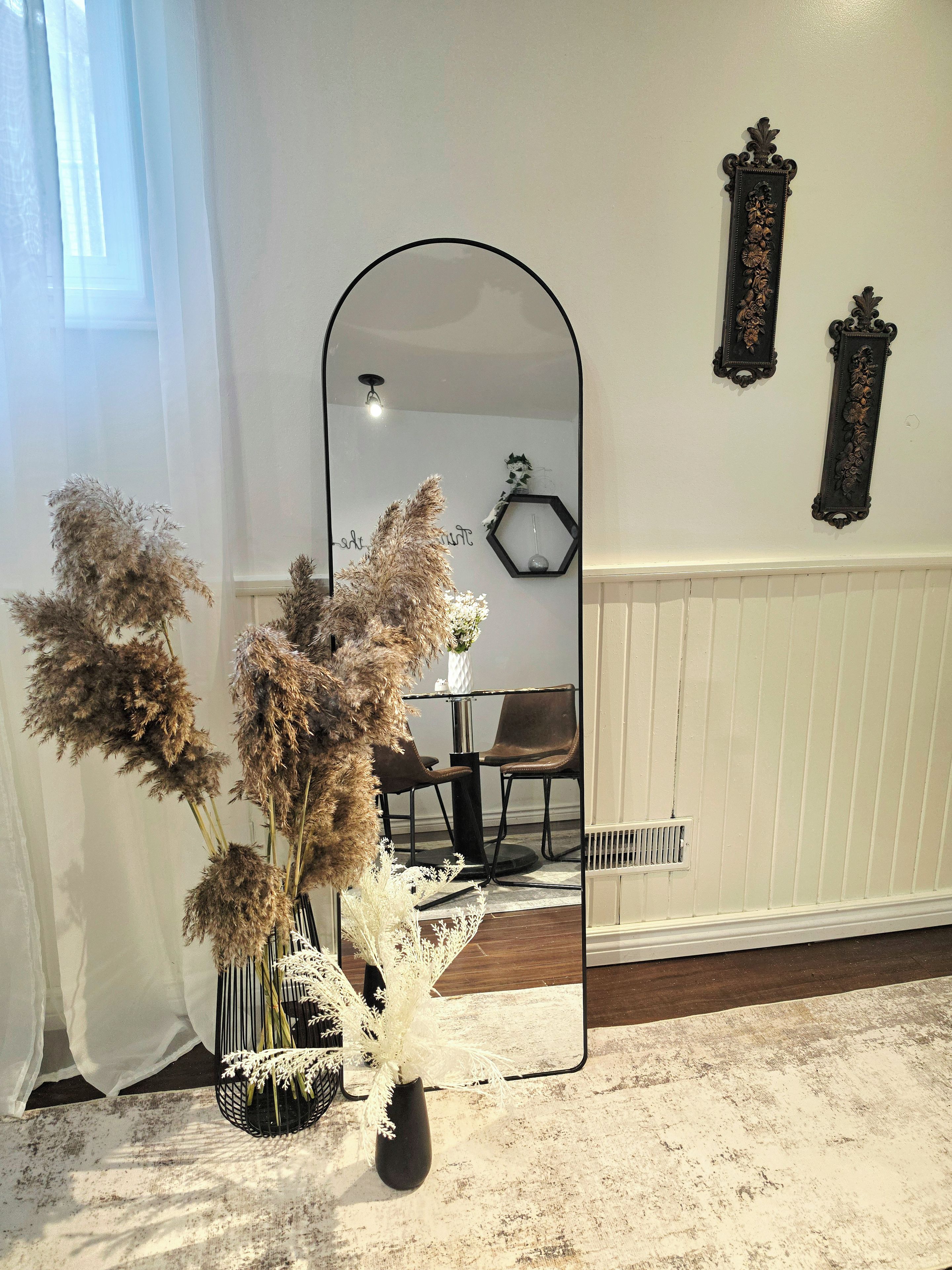 A room with a large mirror reflecting a dining area, a white radiator, and decorative wall pieces.