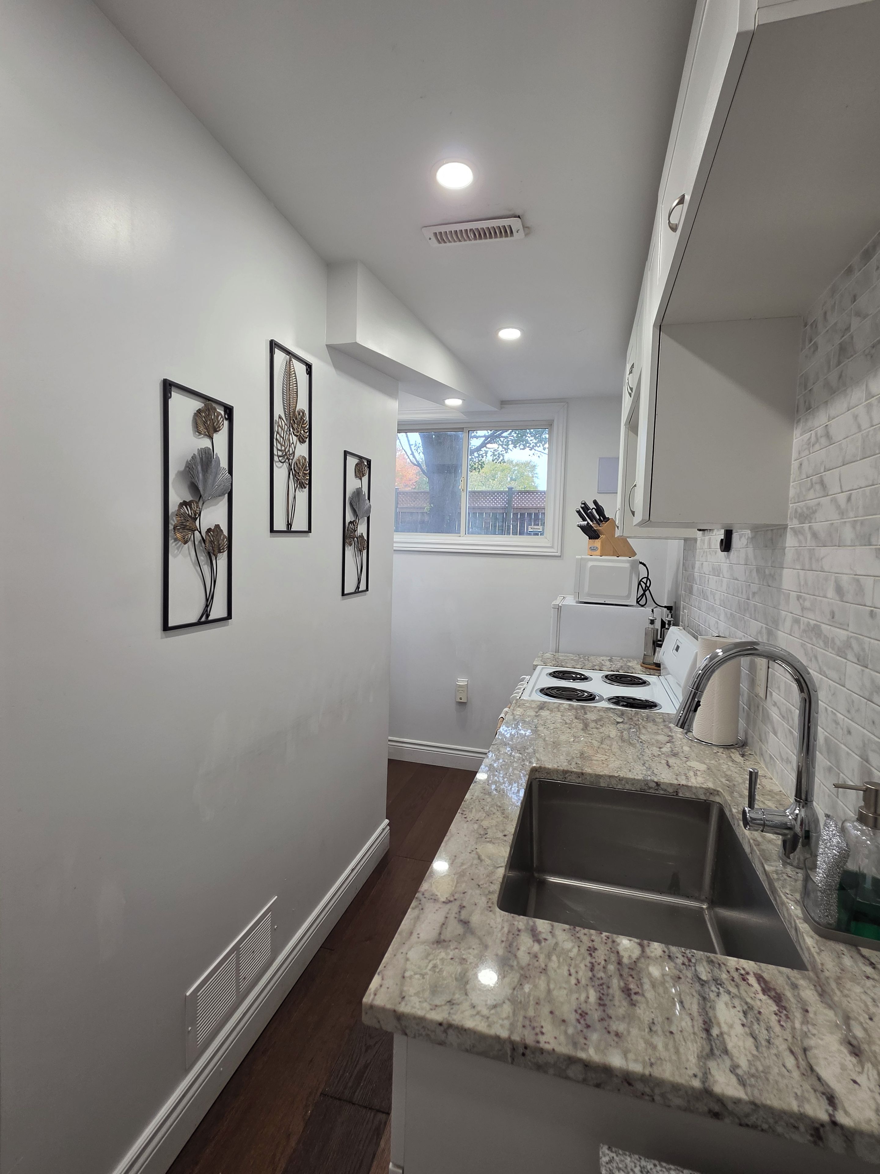A kitchen with white walls, a granite countertop, a stainless steel sink, and a window with a view of the outside.