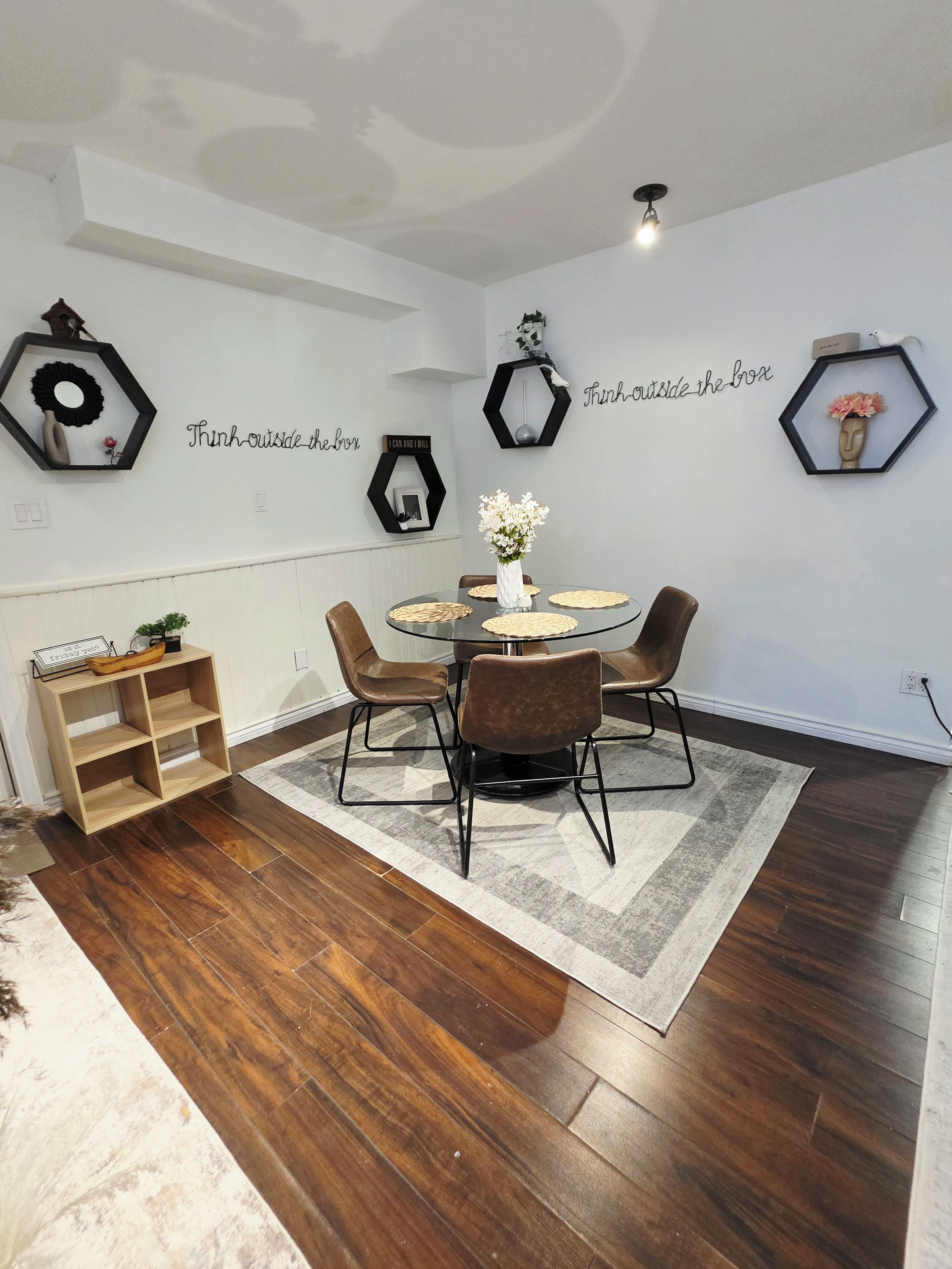 A dining area with a round table, four chairs, a hexagonal wall decoration, and a hexagonal wall decoration with a flower.