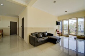 A spacious living area with a dark leather sofa, a wooden door, and a sliding glass door leading to an outdoor balcony. - 77 Guest House By ARBA (Kabupaten Tangerang)