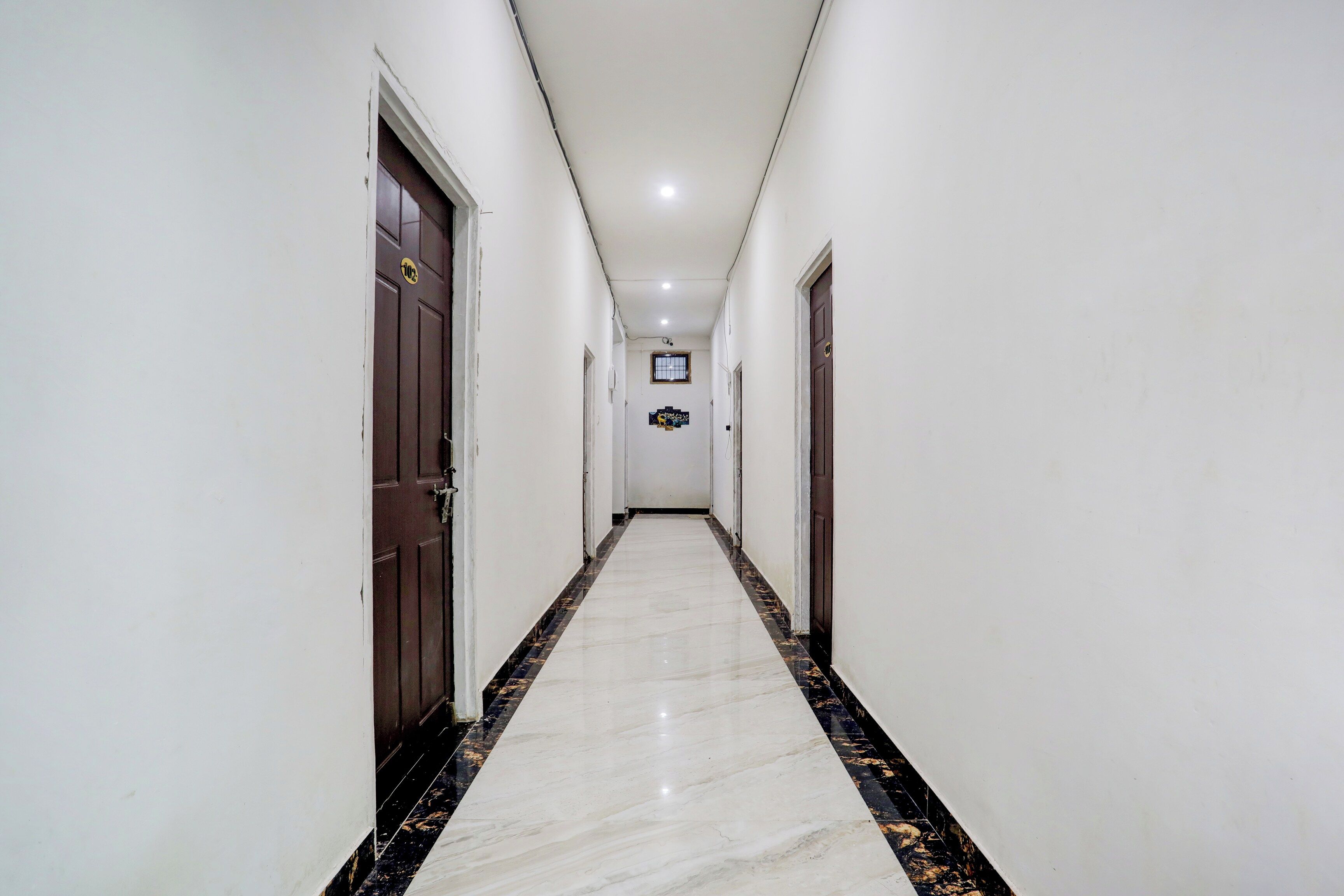 A corridor with white walls, dark wooden doors, and a marble floor with black and gold accents.