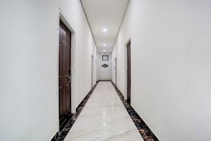 Un pasillo con paredes blancas, puertas de madera oscura y un suelo de mármol con detalles en negro y dorado.