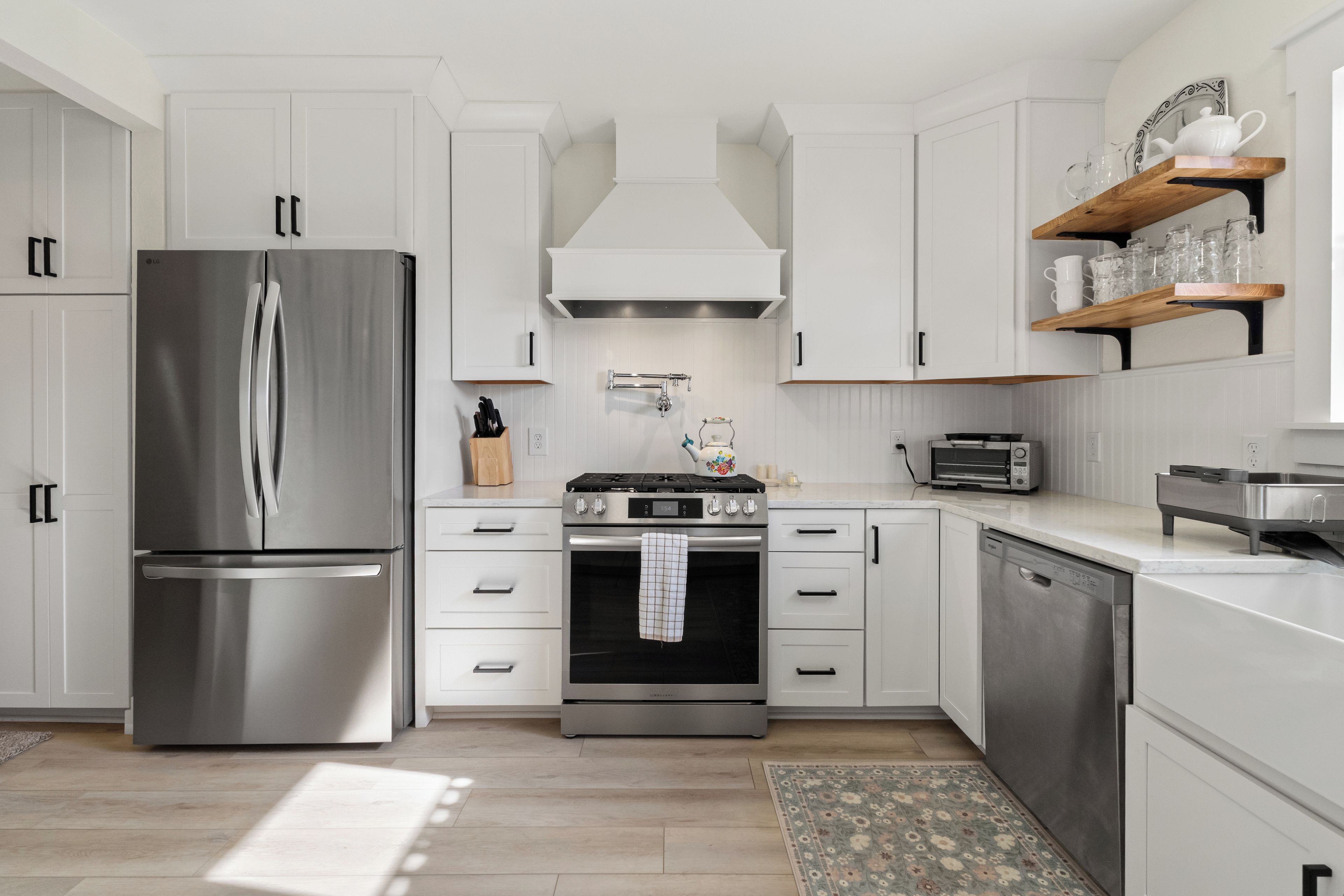 A modern kitchen with white cabinetry, stainless steel appliances, and a wooden floor.