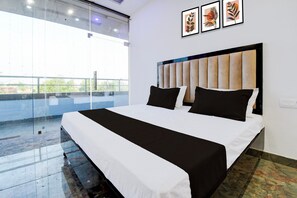 Une chambre d’hôtel avec un grand lit, une vue dégagée grâce à un mur en verre, et trois tableaux encadrés accrochés au mur.