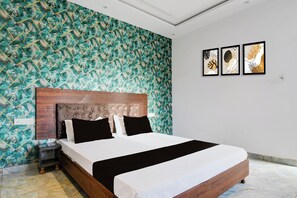 Une chambre à coucher avec un grand lit, une tête de lit capitonnée, un mur à motifs et trois œuvres d’art encadrées accrochées au mur.