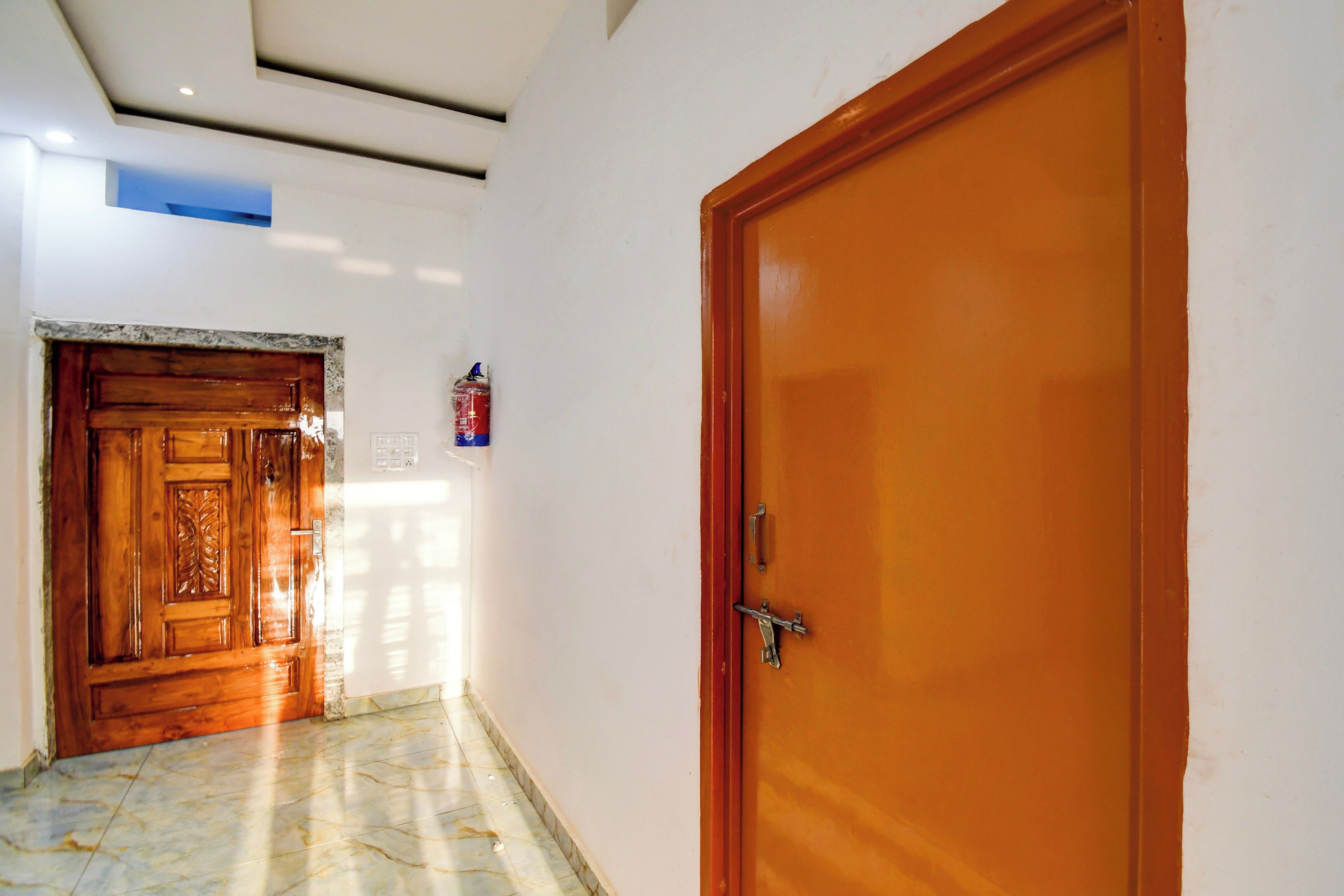 Un couloir avec une porte en bois sur la droite et un sol recouvert de carreaux de marbre.