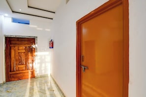 A hallway with a wooden door on the right and a marble-tiled floor. - Hotel O AanandKanan (Varanasi)