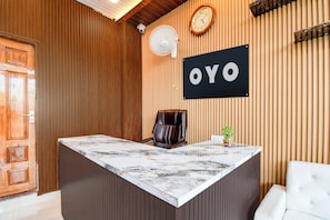 Un comptoir d’accueil avec un plateau en marbre, un fauteuil en cuir, une horloge et une enseigne avec le mot « OYO » sur un mur en bois.