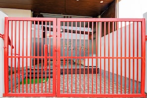 A red metal gate with vertical bars, a tiled floor, and a white wall with a window. - Hotel O AanandKanan (Varanasi)
