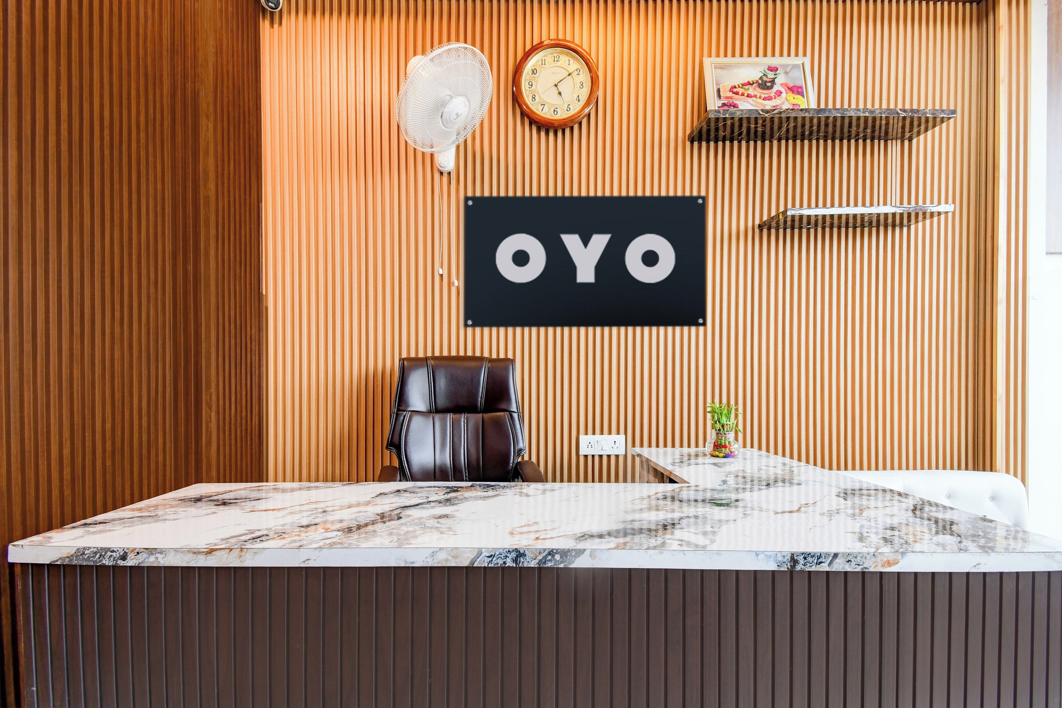 Un comptoir d’accueil avec un plateau en marbre, un fauteuil en cuir noir, une horloge et une enseigne portant les lettres « OYO ».