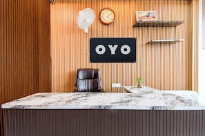 A reception desk with a marble top, a black leather chair, a clock, and a sign with the letters 'OYO'. - Hotel O AanandKanan (Varanasi)