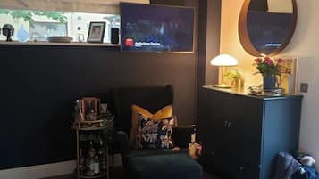 A living room with a dark-colored sofa, a small table with a lamp, a TV on the wall, and a cabinet with a mirror.