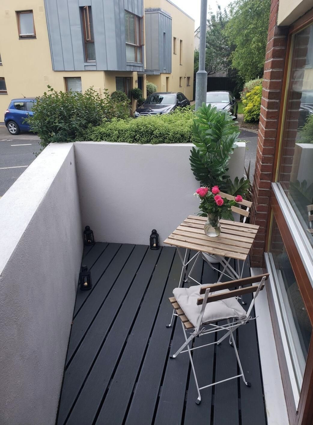 A small outdoor balcony with a table and chairs, a potted plant, and a view of neighboring buildings.