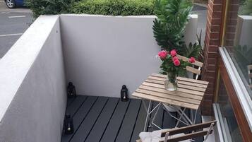 A small outdoor balcony with a table and chairs, a potted plant, and a view of neighboring buildings.