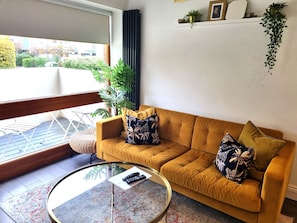 A living room with a sofa, a glass coffee table, and a view of the outside.