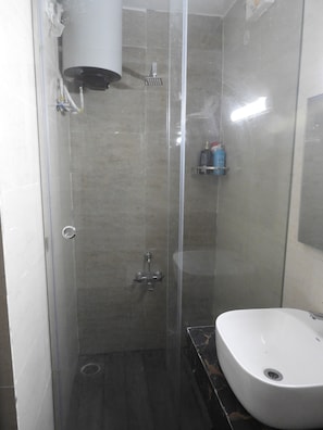 Casa de banho com chuveiro em cabine de vidro, lavatório branco e espelho na parede.