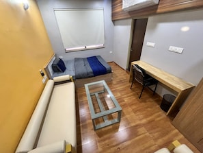 Quarto pequeno com cama, mesinha, sofá e escrivaninha.