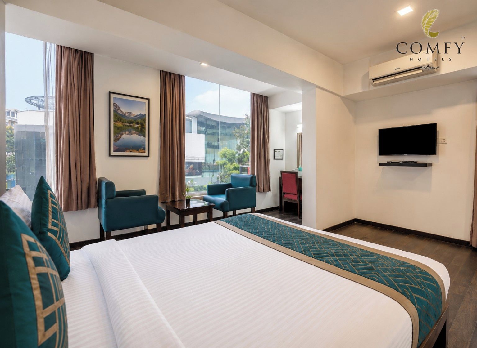 A hotel room with a bed, two armchairs, a small table, a TV, and a large window with curtains.