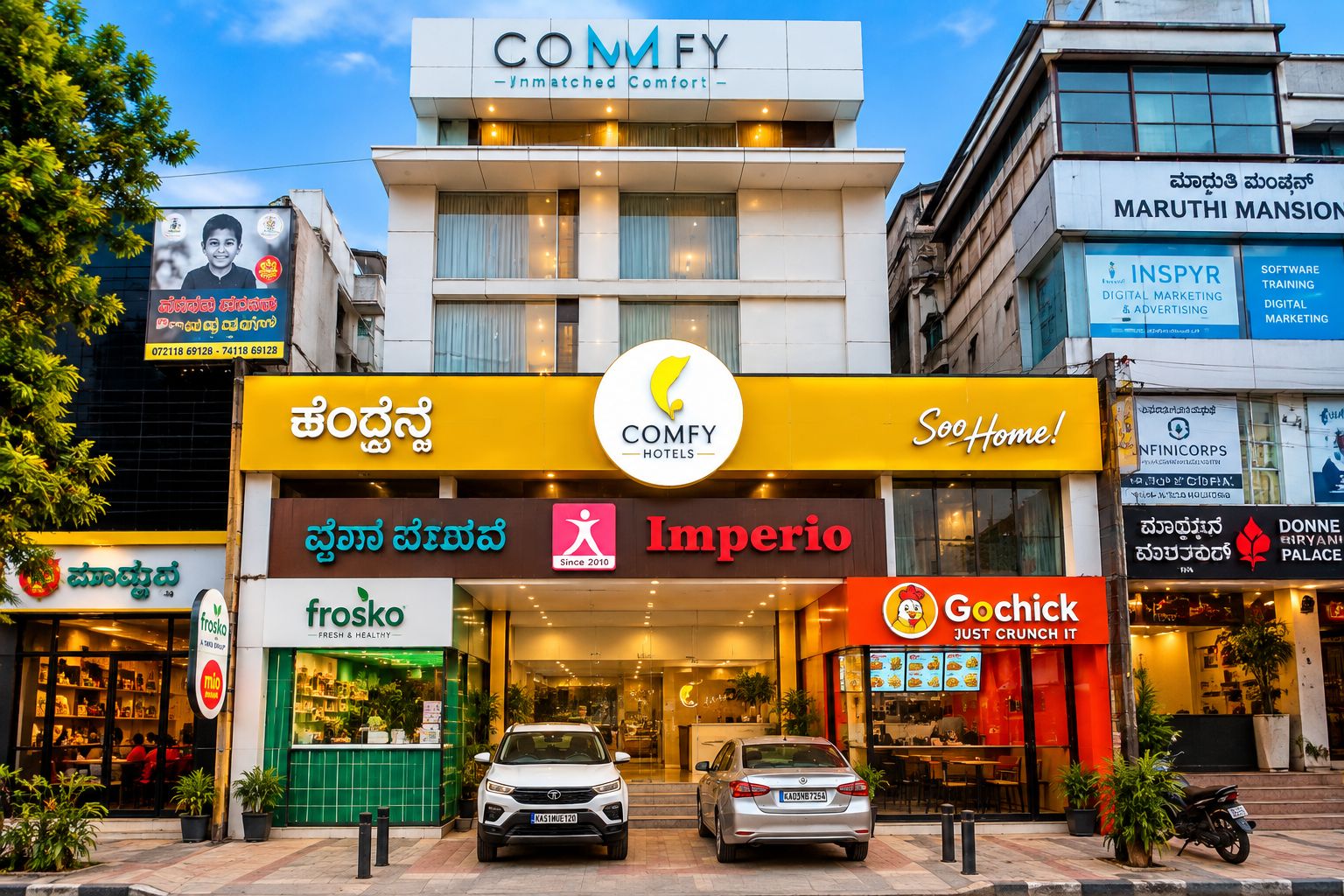 A hotel with a prominent COMFY hotels sign, a visible entrance, and various commercial establishments on the ground floor.