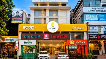 A hotel with a prominent COMFY hotels sign, a visible entrance, and various commercial establishments on the ground floor.