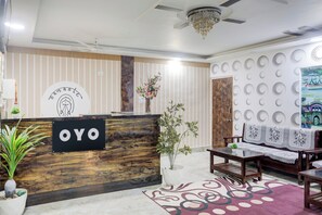 Un espace d’accueil avec un comptoir en bois, une enseigne indiquant « OYO », un lustre, un mur orné de motifs circulaires et un canapé recouvert d’un tissu à motifs floraux.