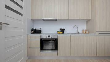 A modern kitchen with light wood cabinetry, a built-in oven, a coffee maker, and a sink.
