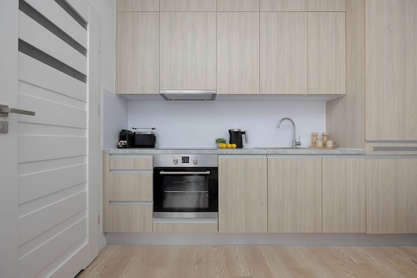 A modern kitchen with light wood cabinetry, a built-in oven, a coffee maker, and a sink. - Warszawa | Krochmalna 61 | Modern Studio | Air Conditioning (Warszawa)