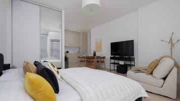 A modern bedroom with a bed, a sofa, a television, and a dining area.