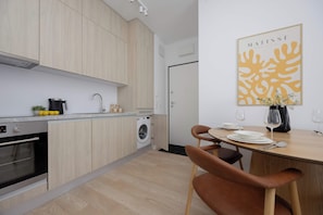 A modern kitchen with wooden cabinets, a built-in washing machine, and a dining area with a table set for two. - Warszawa | Krochmalna 61 | Modern Studio | Air Conditioning (Warszawa)