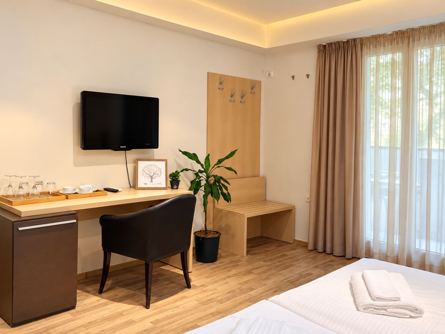 A hotel room with a bed, a desk with a computer, a chair, a television, and a window with curtains.