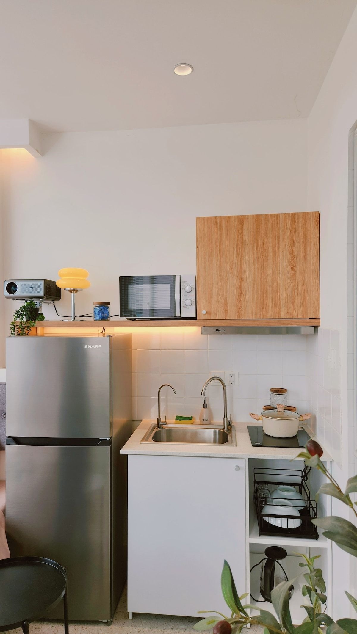 A compact kitchen with a built-in microwave, a stainless steel refrigerator, and a wooden cabinet above the sink.